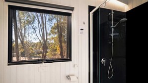 Un baño con ventana que da a árboles, cabina de ducha de vidrio y puerta blanca.