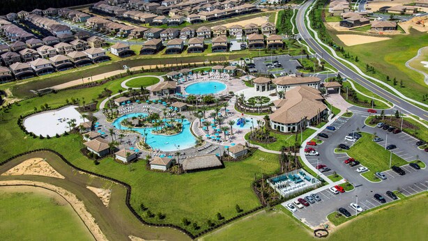 An aerial view of a resort with multiple swimming pools, a parking area, and a large building with a distinctive roof.