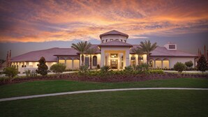 A large, single-story house with a central entrance, surrounded by a well-maintained lawn and palm trees.