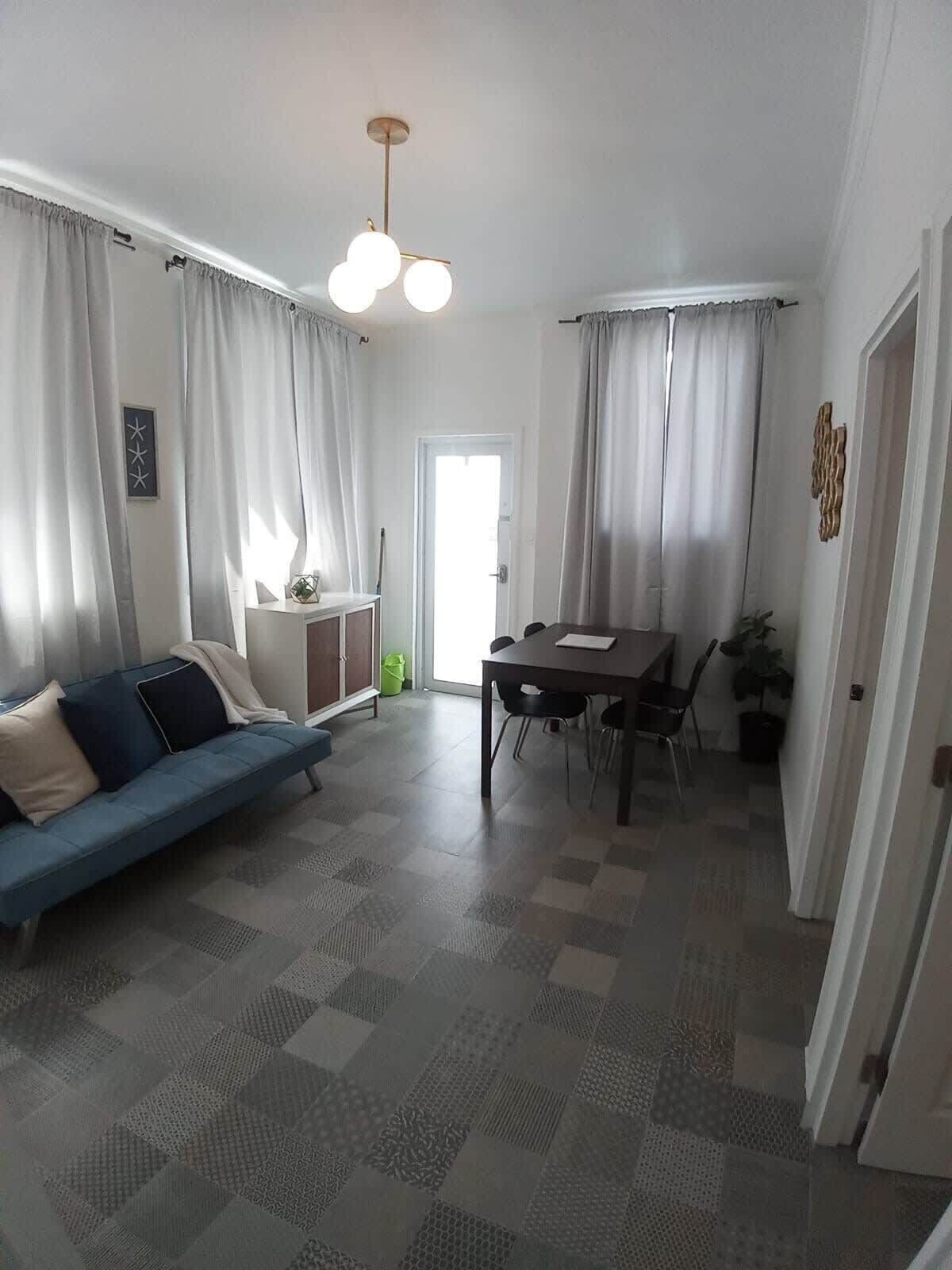 A living room with a sofa, a dining table with chairs, and a ceiling light fixture.