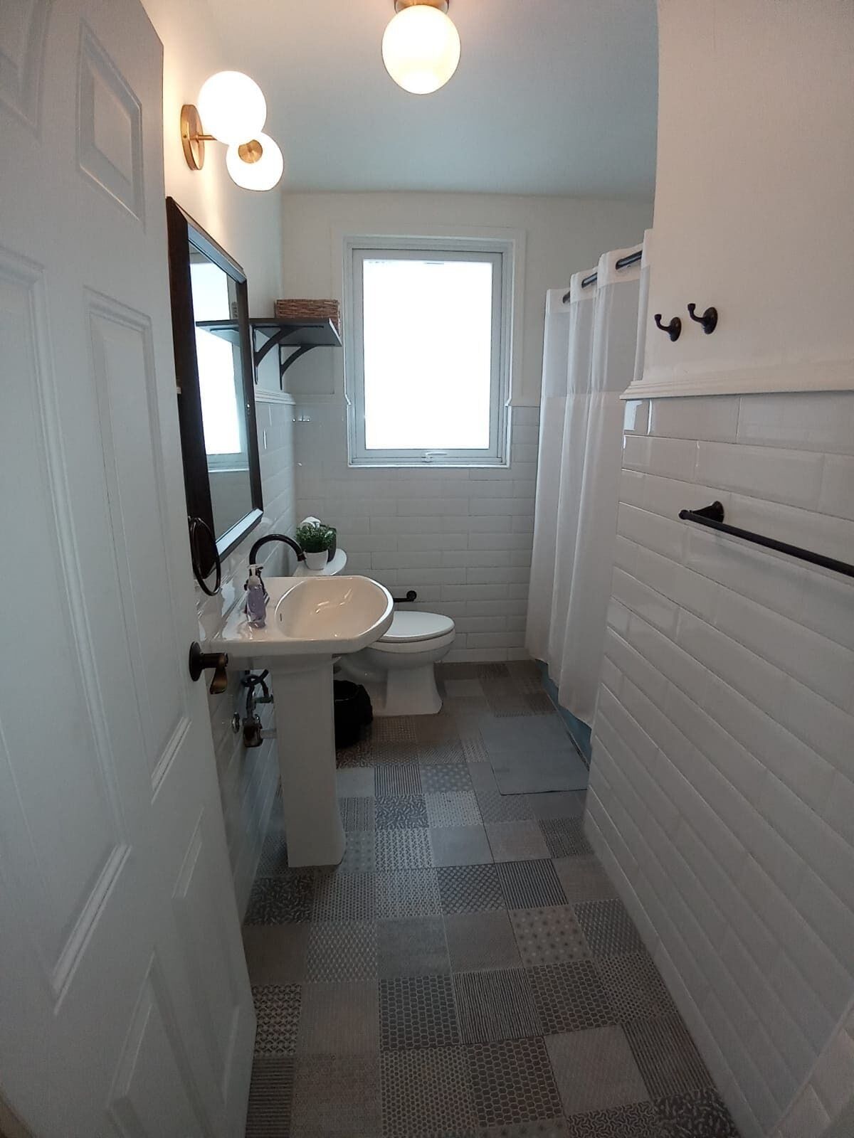 Een badkamer met een wit wastafel, toilet en spiegel. Er is een raam boven het toilet en een handdoekhouder aan de muur.