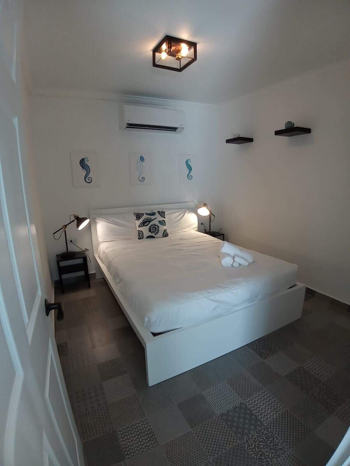 Une chambre à coucher avec un grand lit, deux lampes de chevet, un luminaire au plafond et des œuvres d’art décoratives accrochées au mur.