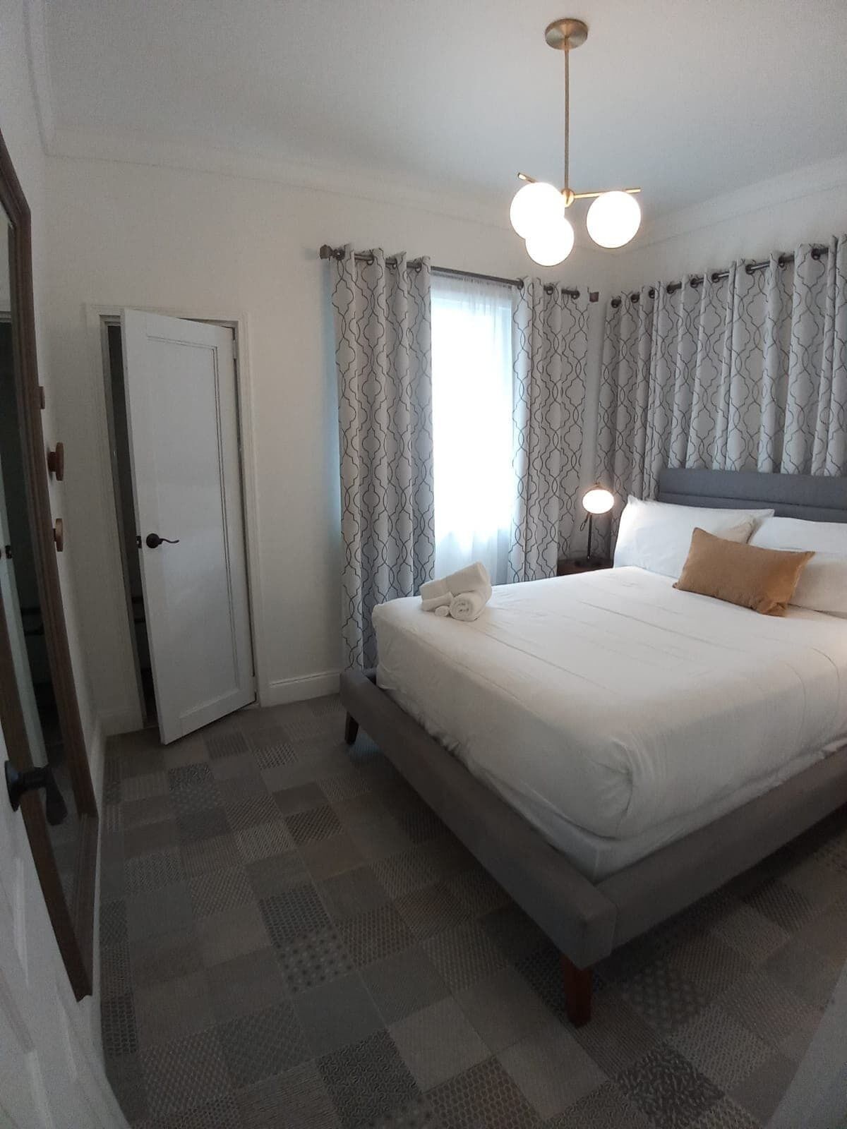 Une chambre d’hôtel avec un lit, une table de chevet avec une lampe, des rideaux à motifs et une porte.