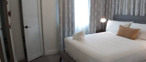 Une chambre d’hôtel avec un lit, une table de chevet avec une lampe, des rideaux à motifs et une porte.