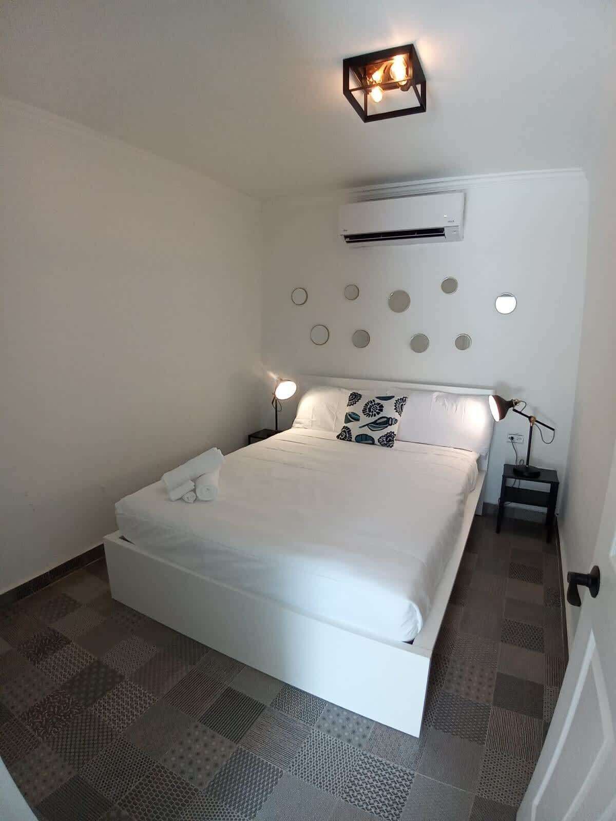 Een keurig opgemaakt slaapkamer met een bed, nachtkastjes en een wandairconditioner.