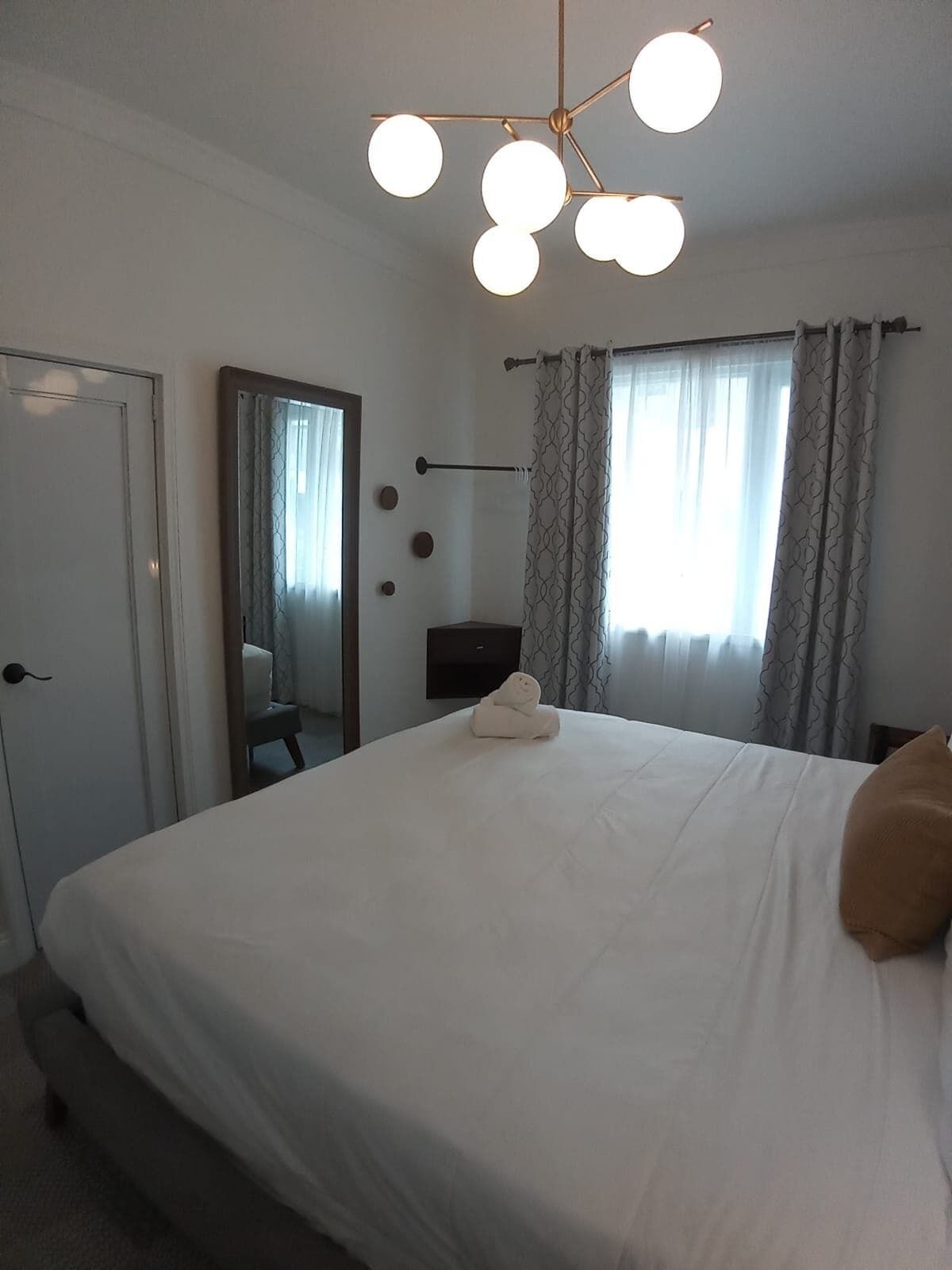 A hotel room with a large bed, a bedside table, a mirror, and a ceiling light fixture.