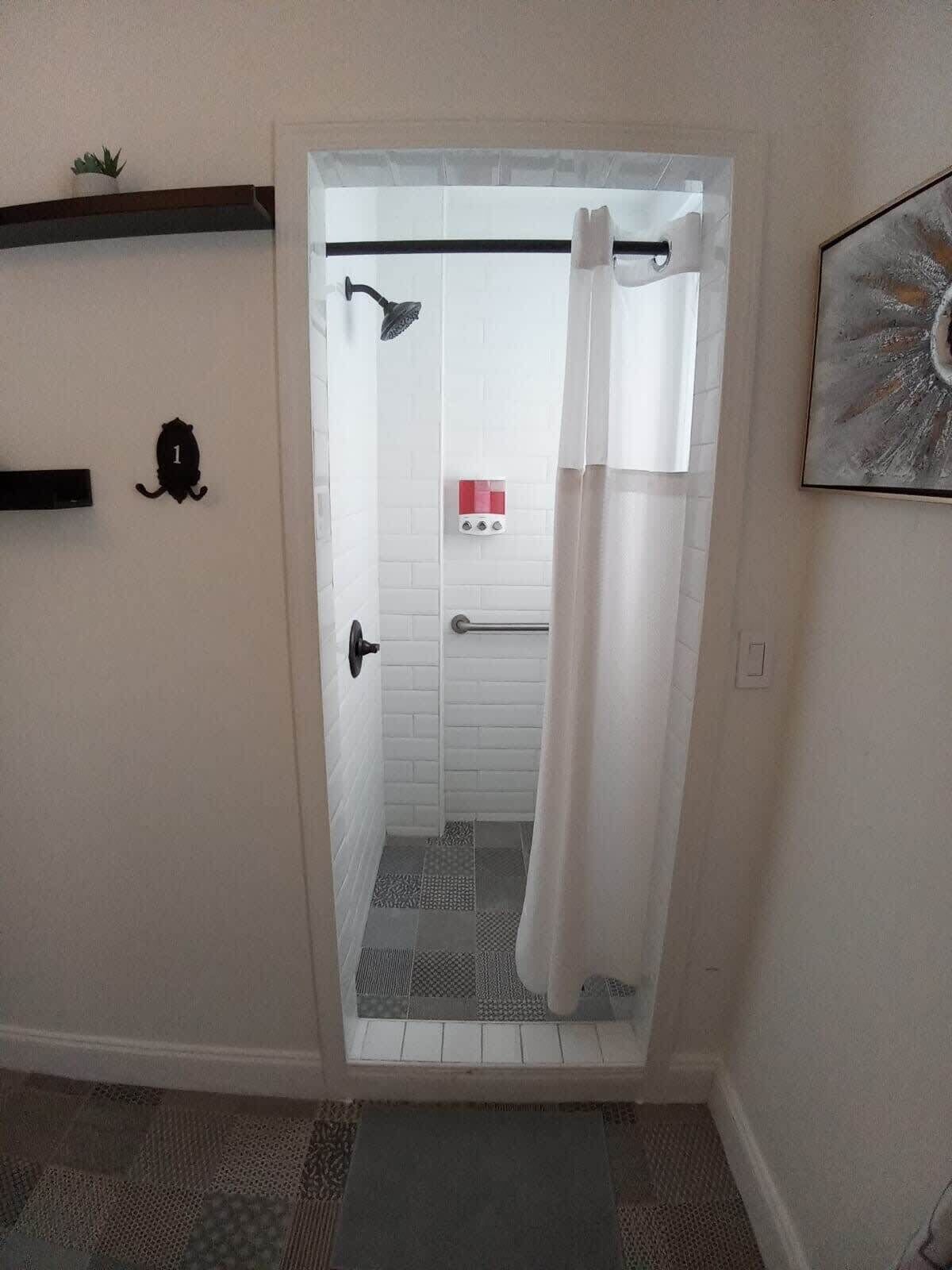 A bathroom with a shower, a towel rack, a potted plant, and a framed picture on the wall.