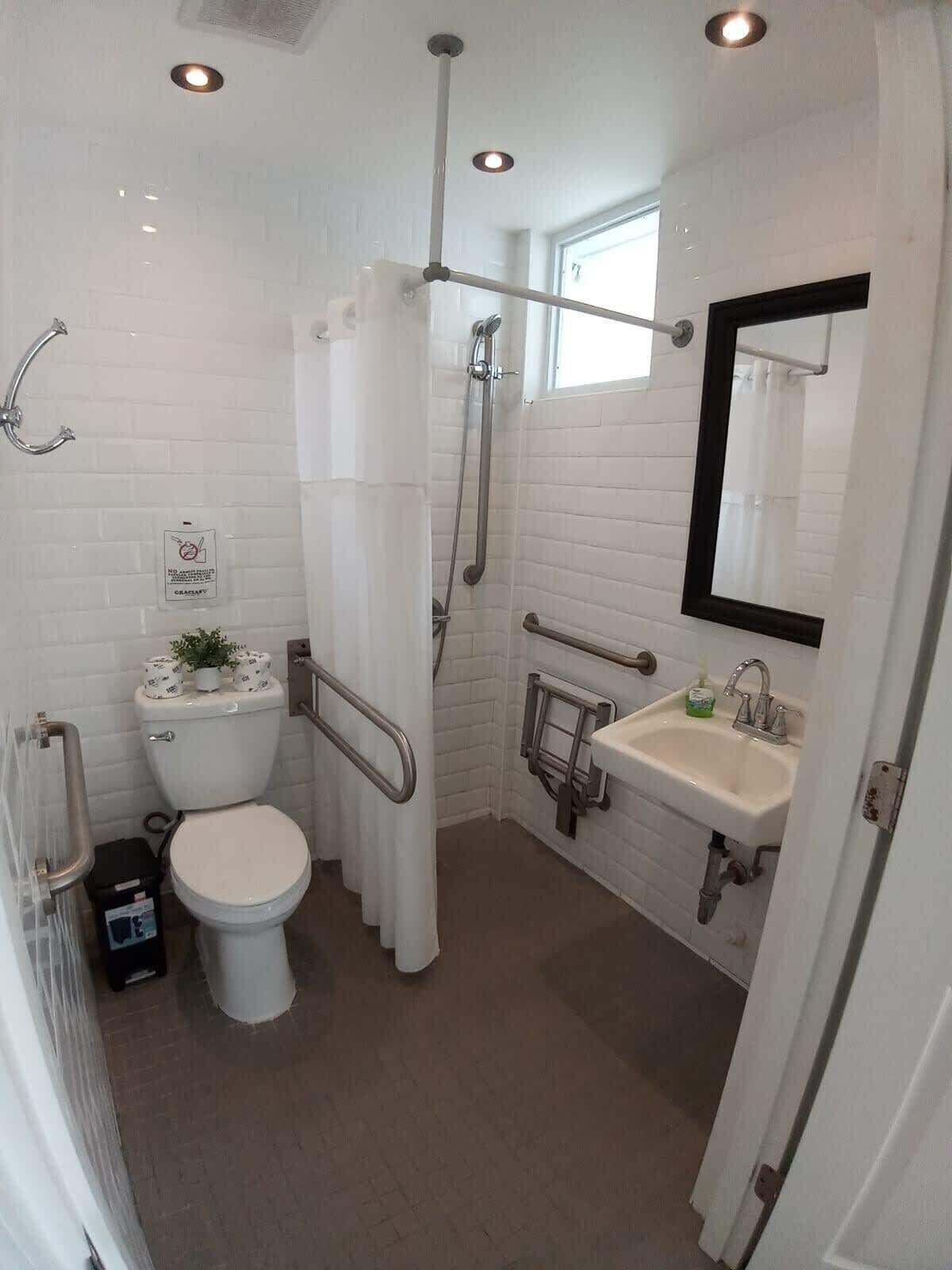 A modern bathroom with a white toilet, a shower with a glass door, a sink with a mirror, and a sign on the wall.
