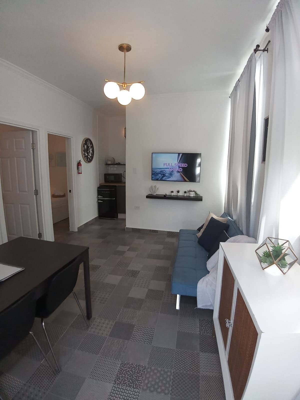 Un salon moderne avec un téléviseur à écran plat, un canapé, une table à manger et un coin cuisine à l’arrière-plan.