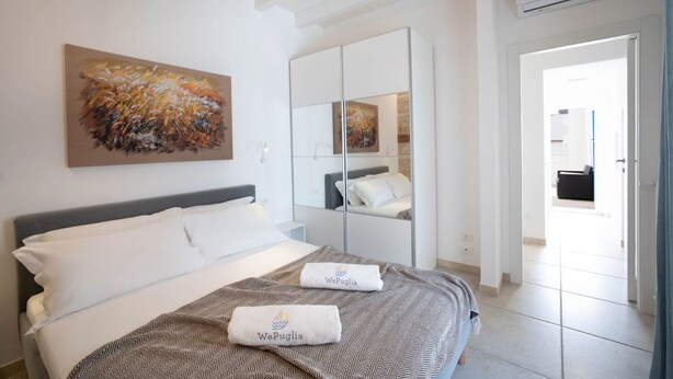 A hotel room with a bed, a large mirror, a painting on the wall, and a view of the outside.