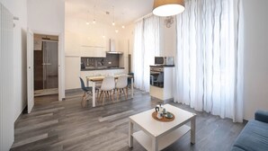 A modern living room with a dining area, kitchen, and a large window with curtains.