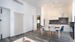 A modern kitchen with white cabinets, a dining area with a white table and chairs, and a visible air conditioning unit.