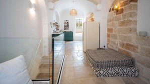 Ein schmales Entree mit Treppe, einer gemusterten Bank und einer Küchenzeile mit Kühlschrank und Regalen.