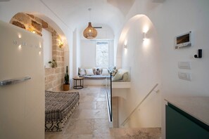 A narrow hallway with a stone wall, a bench, a hanging light fixture, and a staircase.