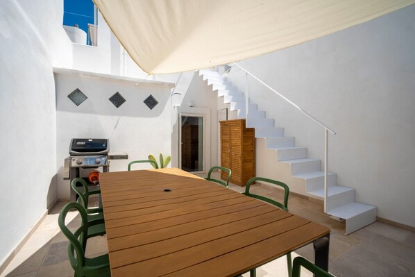 A patio with a wooden table and chairs, a barbecue grill, and a staircase.