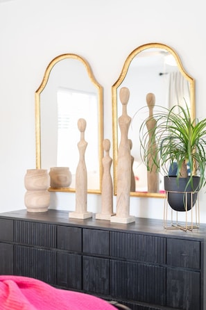 A dresser with a mirror, wooden sculptures, and a potted plant.