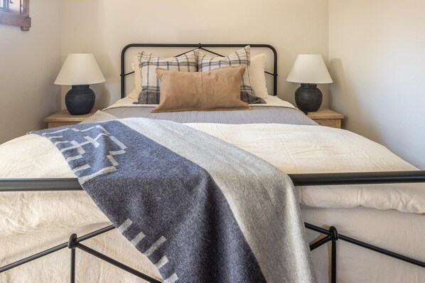 Una cama bien hecha con una colcha gris y blanca, dos lámparas de noche y un cabecero de metal negro.