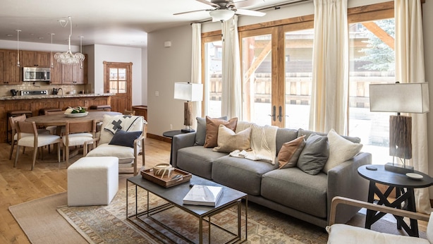 A spacious living room with a grey sofa, a coffee table, and a dining area with wooden furniture. - Town Center | Hot Tub | Ski Shuttle (Big Sky)