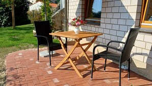 Een terras met een tafel, stoelen, een grote parasol en een bloevas.