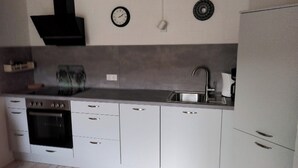 Een moderne keuken met witte kastjes, een inbouwoven, een spoelbak en een zwarte afzuigkap.