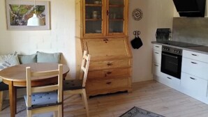 Een kleine keuken met een houten kast, een eettafel met stoelen, een hanglamp en een fornuis.