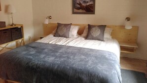 Een slaapkamer met een bed, twee nachtkastjes, een lamp, een foto aan de muur en een houten bankje.