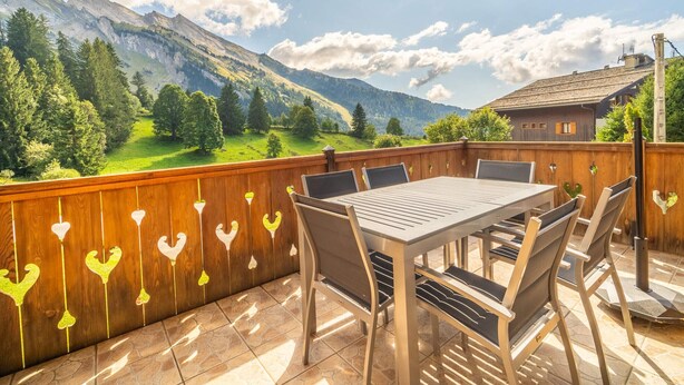 Une terrasse en bois avec une table et des chaises, offrant une vue sur un paysage montagneux.