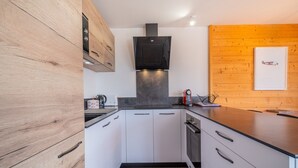 Une cuisine moderne avec des armoires blanches, une hotte noire et un mur d’accent en bois.