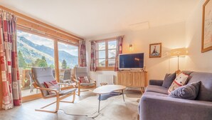 Un salon avec un canapé, des fauteuils, un téléviseur et une vue sur les montagnes.