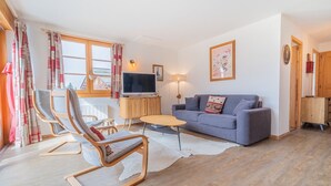 Un salon avec un canapé, un téléviseur, un meuble en bois et une fenêtre avec des rideaux.
