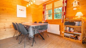 Une cabane en bois avec une table à manger, des chaises, une bibliothèque et une fenêtre avec des rideaux.