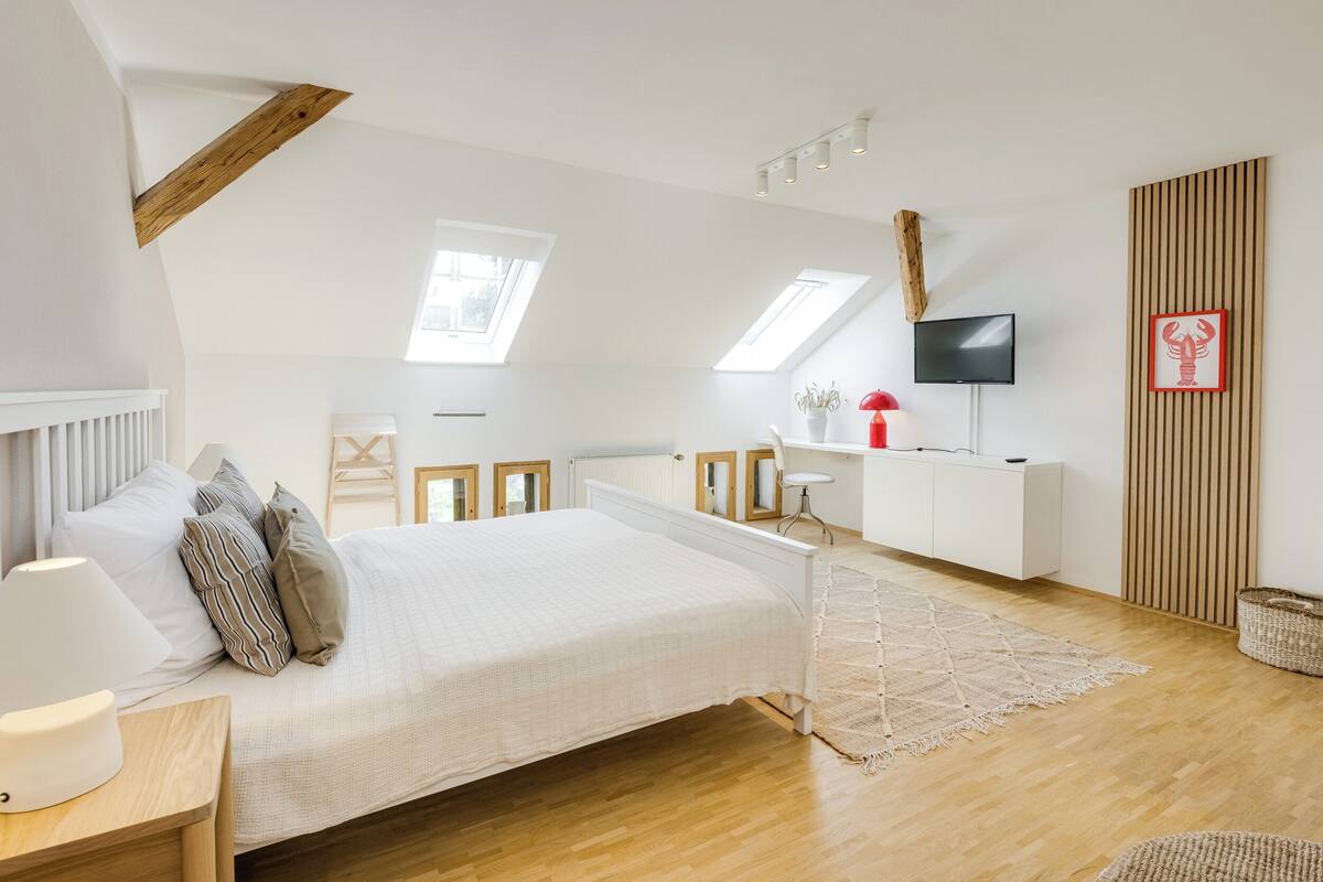 Un dormitorio con techo inclinado, tragaluces, una cama, un escritorio, un televisor y un panel de pared de madera.