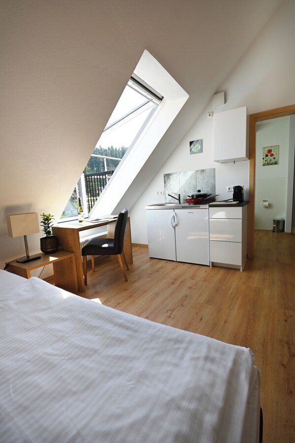 Un dormitorio tipo loft moderno con tragaluces, un escritorio de madera, una silla y una kitchenette.
