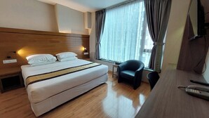 A hotel room with a bed, a desk, a chair, and a window with curtains. - Hotel Grand Galaxy (Yangon)