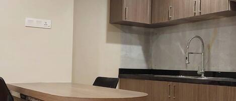 A compact kitchen with wooden cabinets, a stainless steel sink, and a dining area with a wooden table and two chairs.