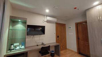 Habitación de hotel con televisor de pantalla plana en la pared, un mueble de madera, un escritorio con silla y una puerta.