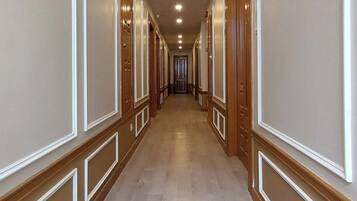 Un lungo e stretto corridoio con porte in legno su entrambi i lati, illuminazione a incasso nel soffitto e un pavimento in legno chiaro.