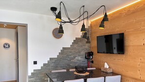 A modern dining area with a stone staircase, a round clock, and a flat-screen TV mounted on a wooden wall.