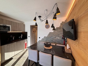 Cozinha moderna com bancada preta, micro-ondas embutido e parede de madeira com uma TV montada.