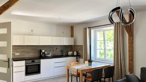 Eine moderne Küche mit weißen Schränken, einer Holzarbeitsplatte und einem eingebauten Ofen. Ein Esstisch mit Stühlen und ein Fenster mit Vorhängen sind ebenfalls vorhanden.