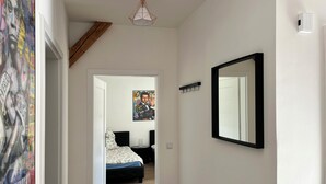 Ein Flur, der in ein Schlafzimmer mit einem Bett, einem Nachttisch und einem Wandspiegel führt.