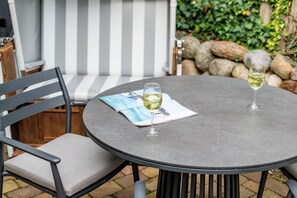 A round outdoor table with a single glass of white wine, a notepad, and a pen.