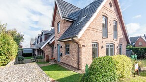 Une maison à deux étages, construite en briques, avec un toit à forte pente, un porche à l’avant et une pelouse bien entretenue.
