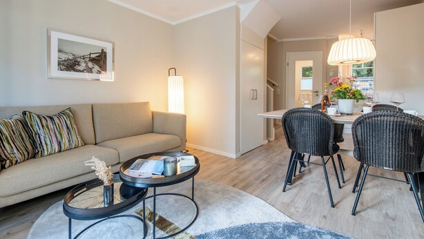 Un salon moderne comprenant un canapé, une table basse et un coin repas avec des chaises.
