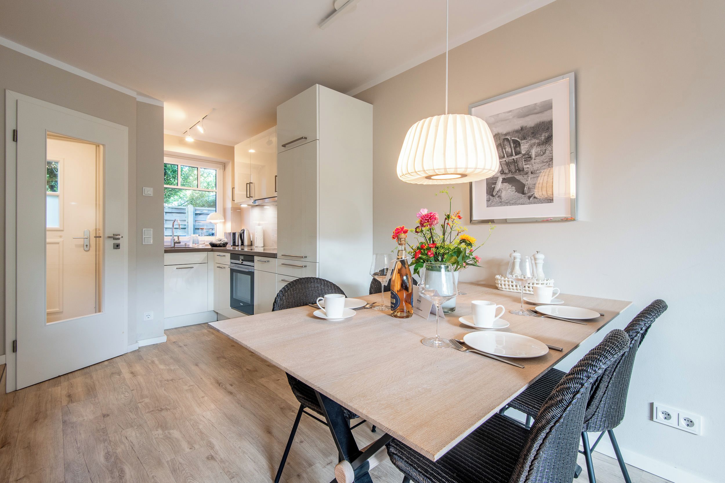 Une cuisine moderne avec des meubles blancs, un coin repas avec une table dressée pour deux personnes et un luminaire suspendu.