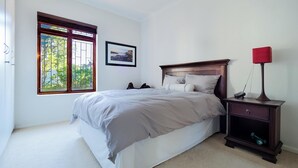 Un dormitorio con cama, mesita de noche, lámpara, ventana con vistas y un cuadro en la pared.