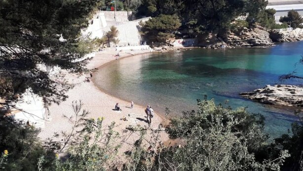 Una playa con agua cristalina, costa rocosa y algunas personas.