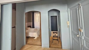 Un pasillo con una cama, un taburete pequeño y una puerta.