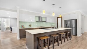 Una cocina moderna con una isla grande, taburetes de bar, electrodomésticos de acero inoxidable e iluminación colgante.