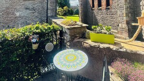 A courtyard with stone buildings, a table with a decorative top, and a rope barrier. - Muddy Boots – Scarpa. (Kirkby Stephen)